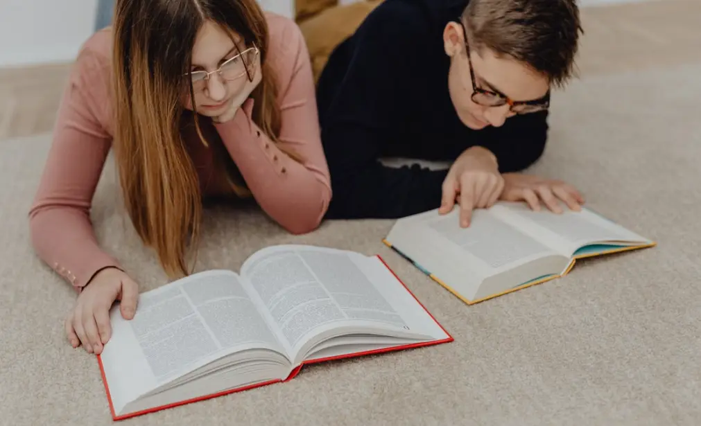 Підлітки лежать на килимі, захоплено читаючи книги, створюючи затишну навчальну атмосферу.